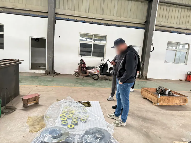 A customer standing over small gears laid out on sheeting, phone in hand, with crated parts behind him.