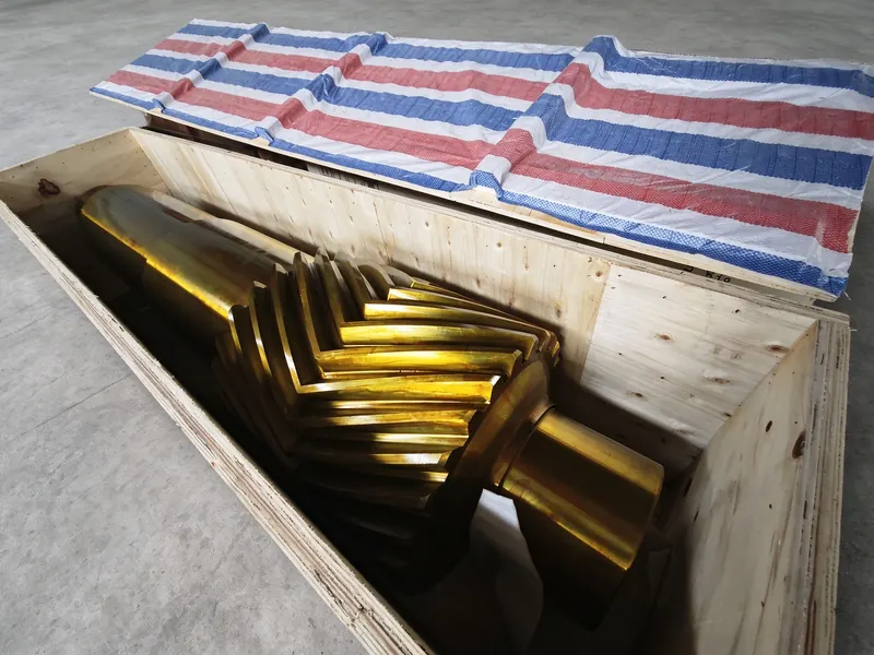 A worm shaft on timber bearers inside an export crate lined with striped tarpaulin.